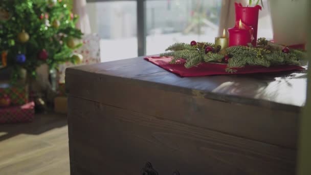 Una corona de hoja perenne con dos velas rojas y una vela dorada. En el fondo, un árbol de Navidad decorado. Las tradiciones y costumbres navideñas de los cristianos en vísperas de la fiesta. — Vídeos de Stock