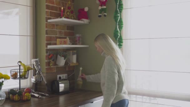 Una joven rubia hermosa entra en la cocina y corrige objetos y varias decoraciones. Navidad — Vídeos de Stock
