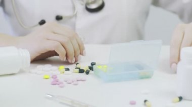 Farklı tabletlerle bir ilaç kutusuna yakın çekim. Bir insan eli ilaç kutusuna koyar.