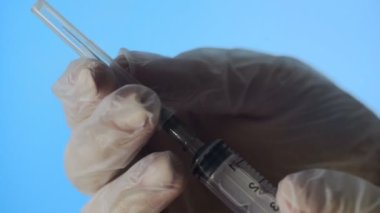 Tek kullanımlık şırınganın iğnesinin yakın çekimi. Küçük bir şırınga sıvıyı mavi arka plandaki delikten dışarı iter.