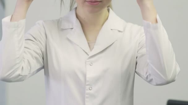 Primer plano de un médico una mujer con una bata médica se pone un estetoscopio en el cuello — Vídeos de Stock