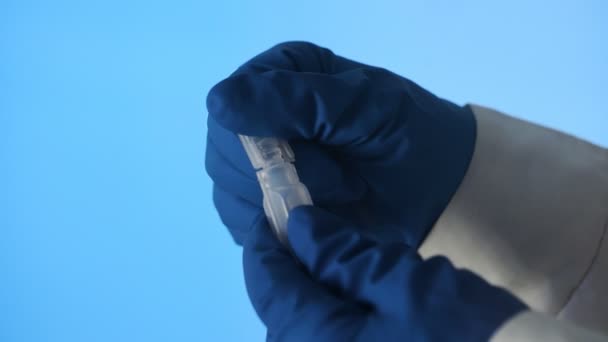 Close-up van een hand in latex handschoenen die een plastic ampul van het vaccin openen op een blauwe achtergrond — Stockvideo