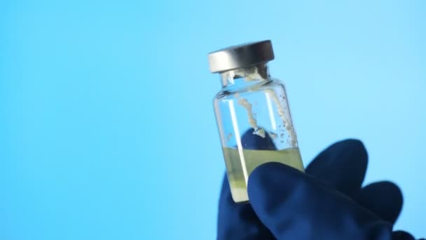 Detailní záběr ruky v latexových rukavicích držících skleněnou ampulku vakcíny na modrém pozadí — Stock video