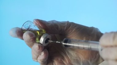 Doktorun elleri mavi arka planda aşı için aşı hazırlıyor.