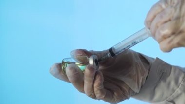 Doktorun elleri mavi arka planda aşı için aşı hazırlıyor.