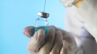 Doktorun elleri mavi arka planda aşı için aşı hazırlıyor.