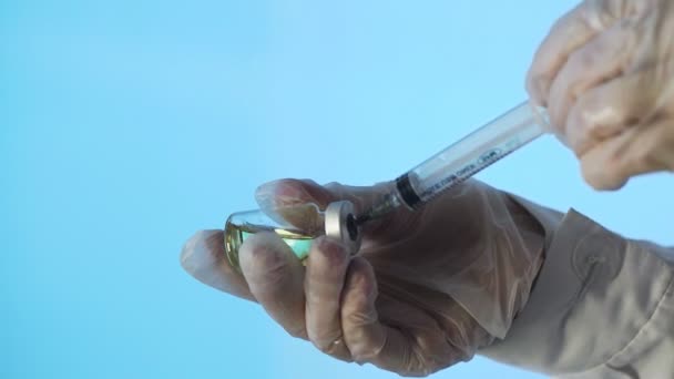 Primer plano de las manos de un médico que prepara una vacuna inyectable sobre un fondo azul — Vídeos de Stock