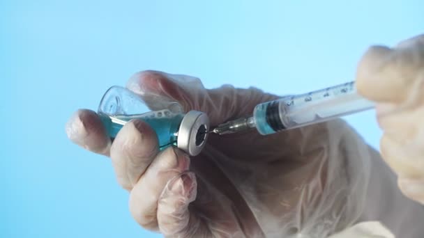 Primer plano de las manos de un médico que prepara una vacuna inyectable sobre un fondo azul — Vídeos de Stock