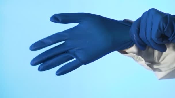 Vrouwenhanden doen een tweede blauwe medische handschoen om hun hand. Close-up op een blauwe achtergrond — Stockvideo