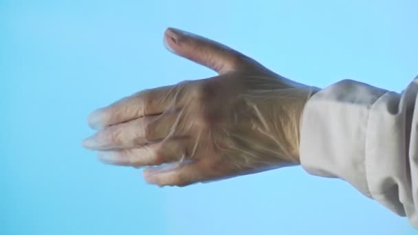 Les mains des femmes mettent un deuxième gant médical transparent sur leur main. Gros plan sur fond bleu — Video