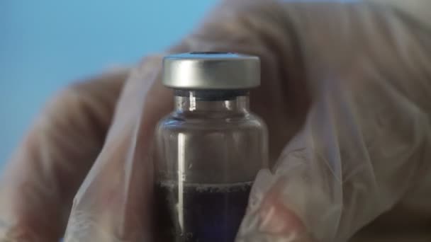 Close-up das mãos dos médicos segurando uma seringa com uma solução transparente e derramando uma substância vermelha em uma ampola. O processo de desenvolvimento de uma vacina, pesquisa experimental em um laboratório médico — Vídeo de Stock