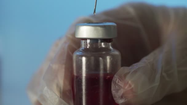 Close-up das mãos dos médicos segurando uma seringa com uma solução transparente e derramando uma substância vermelha em uma ampola. O processo de desenvolvimento de uma vacina, pesquisa experimental em um laboratório médico — Vídeo de Stock