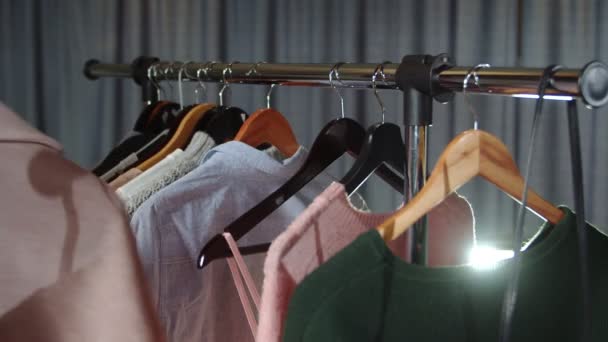 Una tienda de ropa con ropa en perchas. Primer plano. Una mano de mujer cuelga un abrigo beige en una percha — Vídeos de Stock