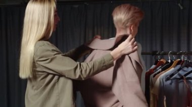 Genç ve güzel bir kadın bir kıza palto giydirir. Genç kadınlar bir giyim mağazasında alışveriş yapıyorlar..