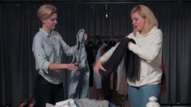 İki mutlu kadın elbiselerini katlıyor, işleri yoluna koyuyorlar.