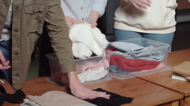 Неузнаваемые женщины выкладывают одежду из пластиковых коробок. Крупный план — стоковое видео