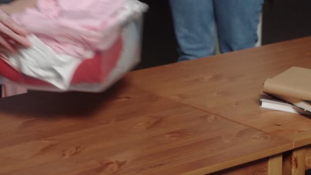 Μια αγνώριστη γυναίκα βάζει ένα πλαστικό κουτί με ρούχα στο τραπέζι. Κοντινό πλάνο — Αρχείο Βίντεο