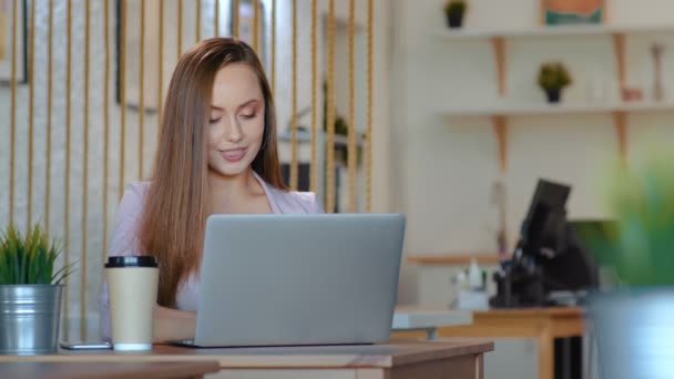 Een jonge vrouw zit achter een computer in het kantoor en trekt haar haar recht kijkend naar de camera — Stockvideo