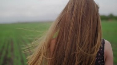 Çiçek baskı ile koyu elbiseli güzel sağlıklı kadın durumda ve yeşil tarlada çalışan geriye dönüp saç yakın çekim esen rüzgar