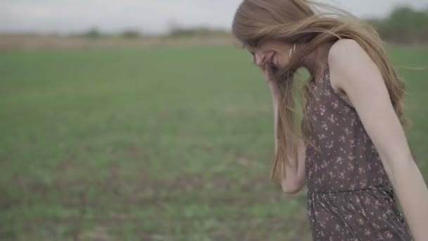 Красива дівчина зі стрічкою в темній сукні з квітковим принтом біжить через зелене поле, а вітер, що дме, обертається, слідує від взуття до волосся середнього пострілу немодернізованого плоского кольору — стокове відео