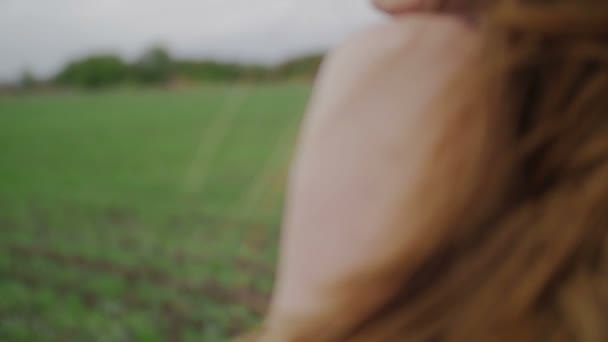 Floral nyomtatási sötét ruha gyönyörű egészséges nő áll, és aztán futás zöld mezőn tekint vissza, és a szél fúj haját szoros lövés — Stock videók