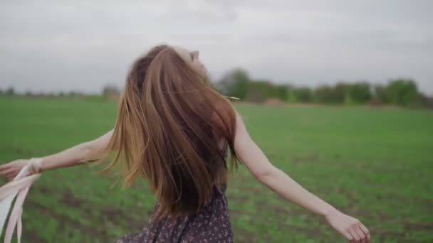 Счастливая молодая женщина в темном платье с цветочным принтом весело проводит время на открытом воздухе в джинсовом поле. Красавица кружится и смеется. — стоковое видео