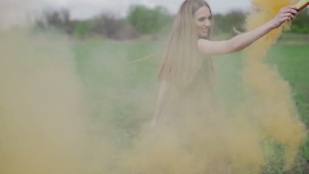 Mujer joven feliz en vestido oscuro con estampado floral que se divierte al aire libre en el campo geen. Chica de belleza con naranja bomba de humo girando y riendo.sonrisa maravillosa. fondo verde humo colorido lento — Vídeos de Stock