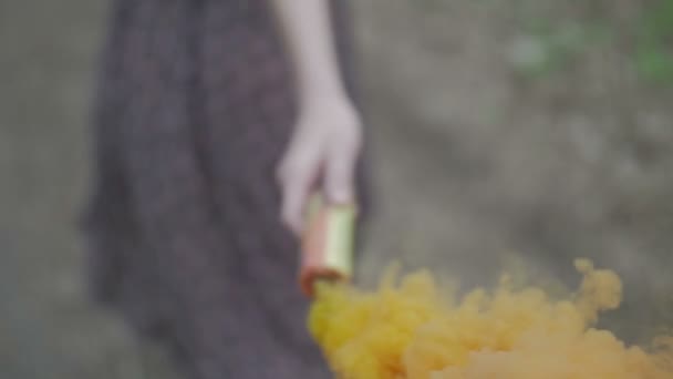 Szczęśliwa młoda kobieta w ciemnej sukni z kwiatowym nadrukiem zabawy na zewnątrz w pomarańczowy kolorowy dym. Piękna dziewczyna trzyma barwną pomarańczową bombę dymną. wspaniały uśmiech. Kamera podąża z bliska w zwolnionym tempie — Wideo stockowe