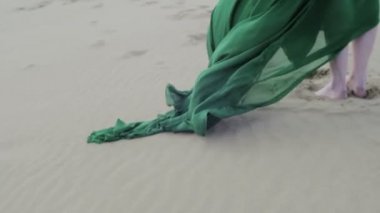 Yeşil elbiseli güzellik kız ayağa kumul üzerinde iken giysiler yavaş ayağını esen rüzgar yakın çekim