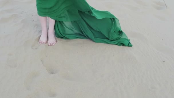 Menina beleza no vestido verde stand na duna de areia, enquanto o vento soprando suas roupas câmera lenta pé vista frontal de perto — Vídeo de Stock