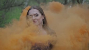 Mutlu genç kadın çiçek Yazdır açık yaz ormanda eğleniyor ile koyu elbiseli. Güzellik kız renkli portakal duman bombası holding ve camera.wonderful gülümseme gider. Orta yakın yavaş yukarı
