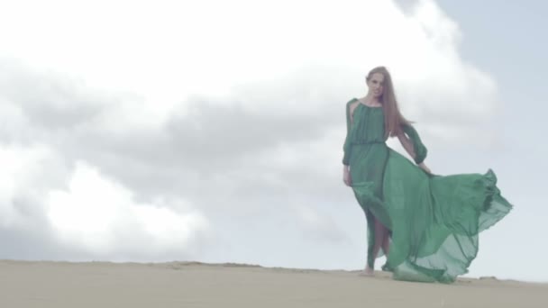 Girl stand in green dress on sand dune while wind blowing her clothes slow motion sky background figure shot ungraded flat color — Stock Video