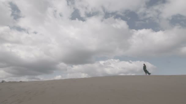 Schoonheid meisje in groene jurk stand op zand-duin terwijl wind waait haar kleren slowmotion hemel achtergrond long shot ongesorteerde egale kleur — Stockvideo