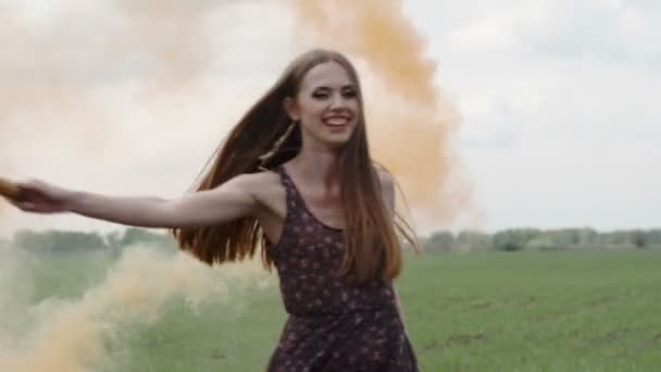 Mujer joven feliz en vestido oscuro con estampado floral que se divierte al aire libre en el campo geen. Chica de belleza con bomba de humo naranja girando y riendo. medio largo tiro cámara lenta — Vídeos de Stock