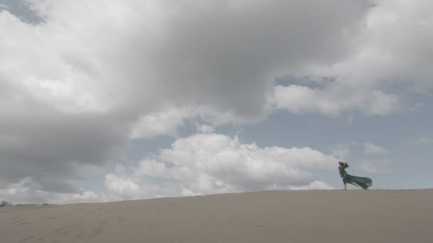 Belleza Chica en vestido verde corriendo en la duna de arena, mientras que el viento soplando su ropa cámara lenta cielo azul largo tiro sin clasificar color plano — Vídeos de Stock