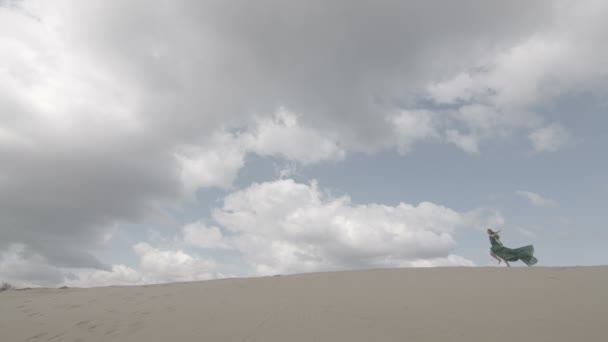 Beauté Fille en robe verte fonctionnant sur une dune de sable tandis que le vent soufflant ses vêtements au ralenti ciel bleu long plan couleur plate non dégradée — Video