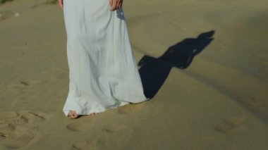 Güneş gölge yavaş damla iken beach kumulları beyaz elbiseli üzerinde yürüyen kadın ayakları