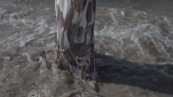 Frauen steht in weißem Blumenkleid am Meeresstrand in Wellenschaum am sonnigen Sommertag flache Farbe — Stockvideo