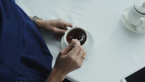 Una mujer en un vestido azul agita el café con una cuchara en una mesa blanca — Vídeo de stock