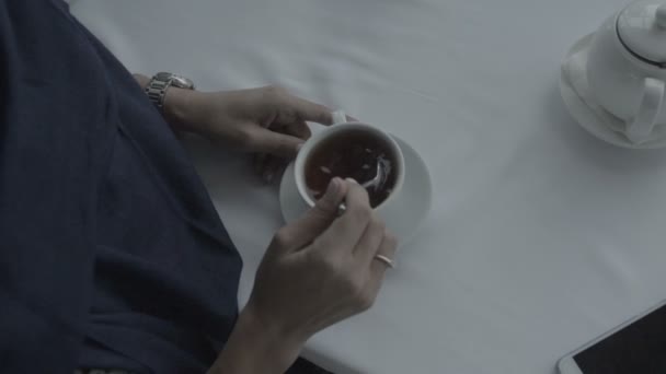 Una mujer en un vestido azul agita el café con una cuchara en una mesa blanca de color plano — Vídeo de stock