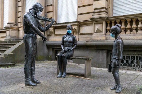 Bonn, Nordrhine-Westfalia, Germany, 07 10 2020: 'Violinist with woman and child' (Geiger mit Frau und Kind) statue/sculpture in Bonn Bad Godesberg decorated with filtering facepiece (FFP).