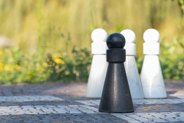 Four Life-Sized Pawns on a Chess Board, three white pawns and one black in front, focus on the black pawn