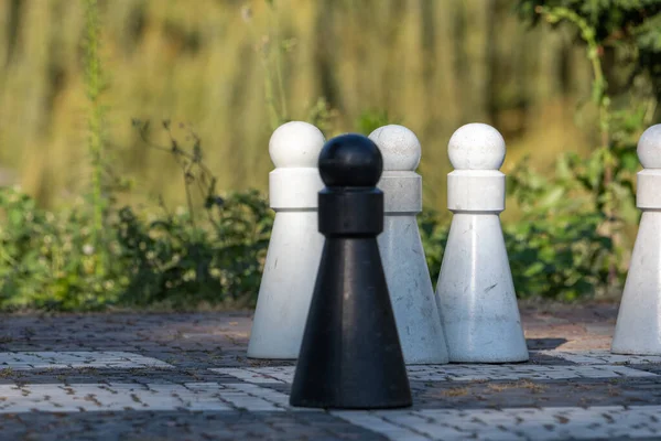 Four Life-Sized Pawns on a Chess Board, three white pawns and one black in front, focus on the white pawns