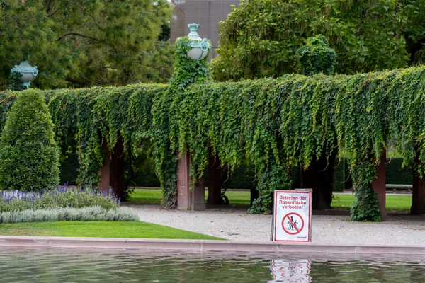 Mannheim, Baden-Wuerttemberg, Germany, 09 25 2020 Sign saying 'Betreten der Rasenflaeche verboten' (trespassing on the grass is prohibited) with water in the foreground and hedge in the background