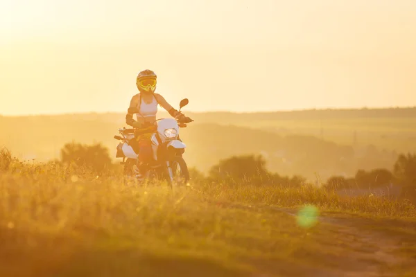 Γυναίκα ποδηλάτης στο ηλιοβασίλεμα, θηλυκό μοτοσικλέτα. — Φωτογραφία Αρχείου