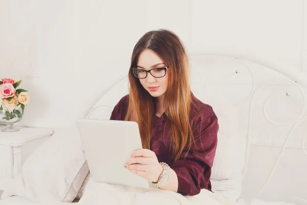 Jovem mulher lê a partir de tablet pc na cama, chave alta — Fotografia de Stock