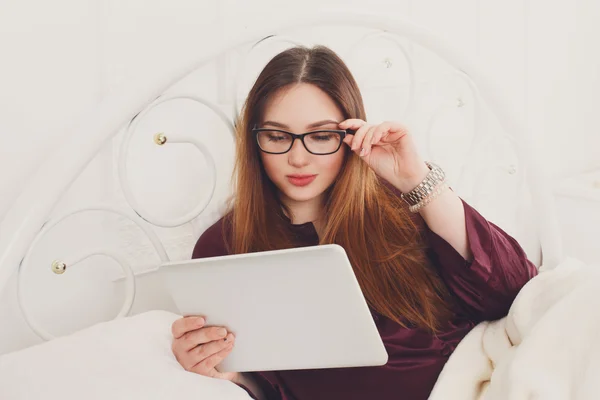 Jovem mulher lê a partir de tablet pc na cama, chave alta — Fotografia de Stock