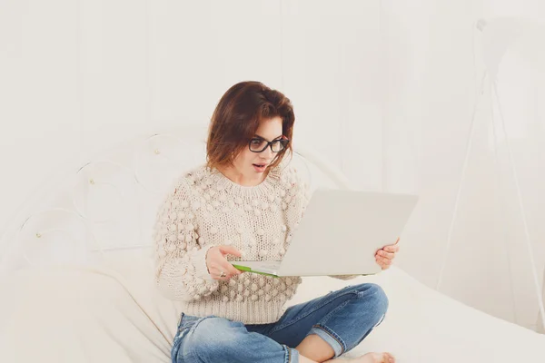 Giovane donna legge dal computer portatile a letto, chiave alta — Foto Stock
