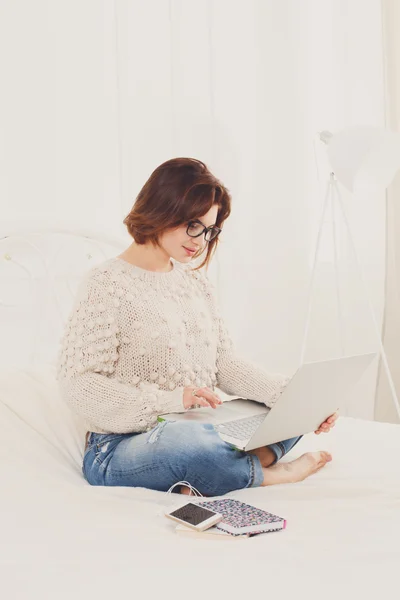 Jovem mulher lê a partir de laptop na cama, chave alta — Fotografia de Stock