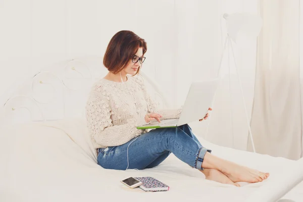 Молодая женщина читает с ноутбука в постели, высокий ключ — стоковое фото
